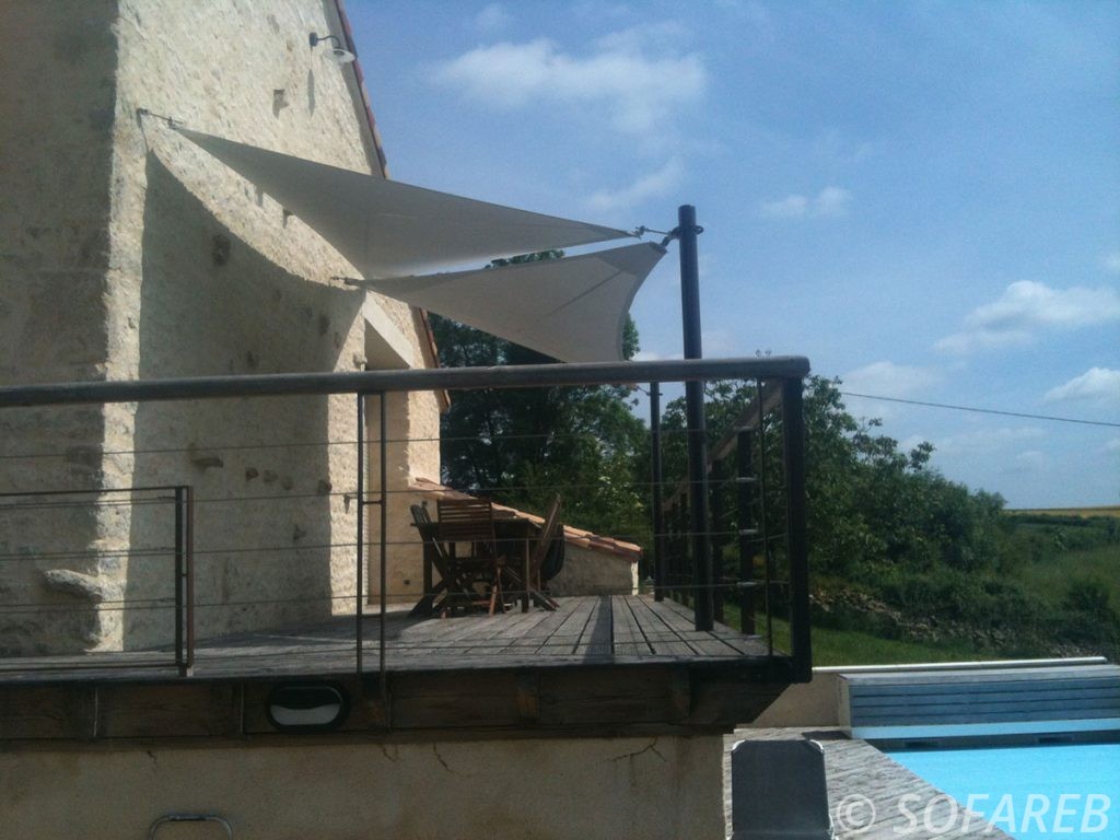 Voiles d'ombrage posées au dessus de la terrasse en bois surélevé d'une maison, avec une piscine en contrebas