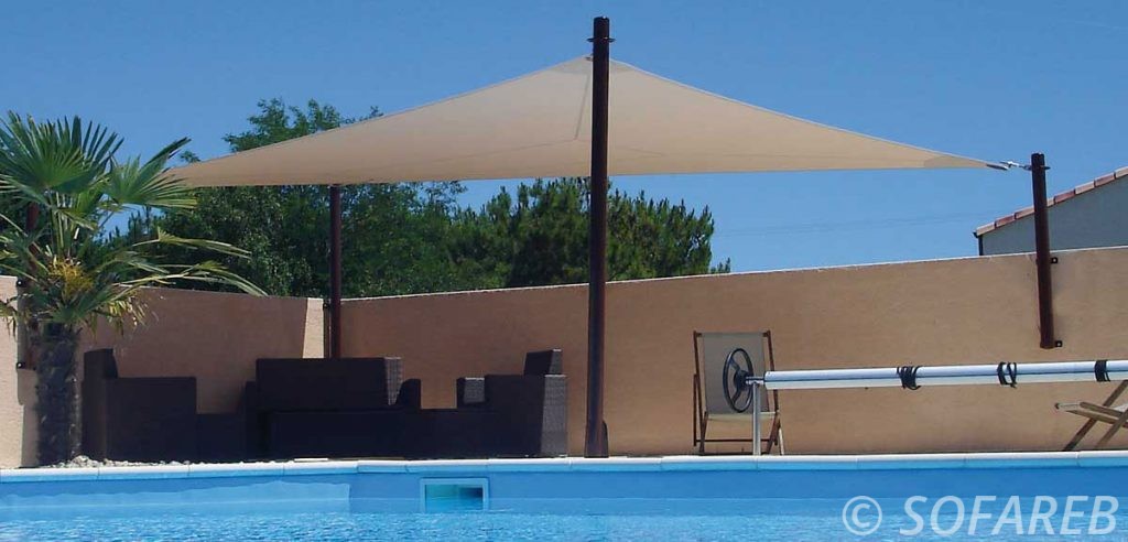 voile dombrage triangulaire de couleur beige avec des attaches sur-mesures posées devant une piscine par l-équipe sofareb