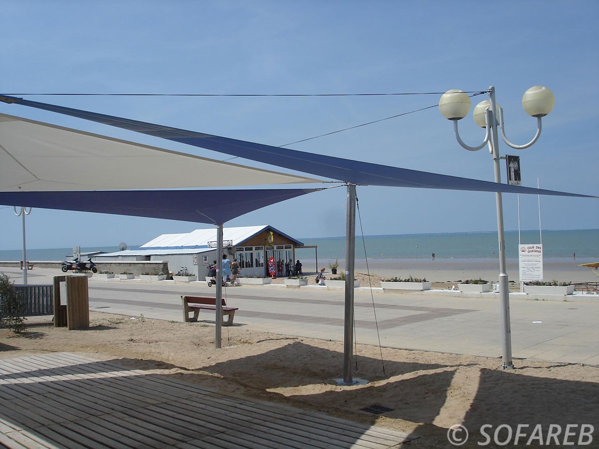Voiles dombrage triangulaires grand format et de qualité installées au dessus de la terrasse d'un restaurant situé au bord de la mer