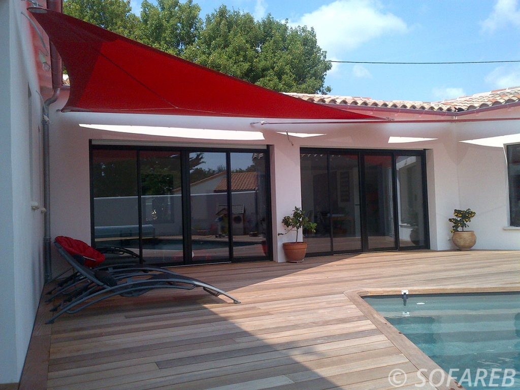 Voiles dombrage triangulaire rouge design fabriquée avec des tissus Serge Ferrari et accrochée au dessus de la terrasse en bois dune maison contemporaine