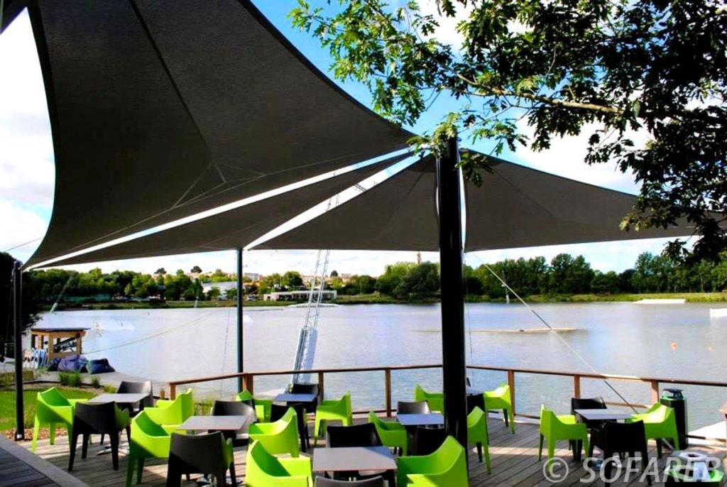 Trois grandes voiles d-ombrage noires anti-uv qui couvre la terrasse d-un restaurant pres d-un lac
