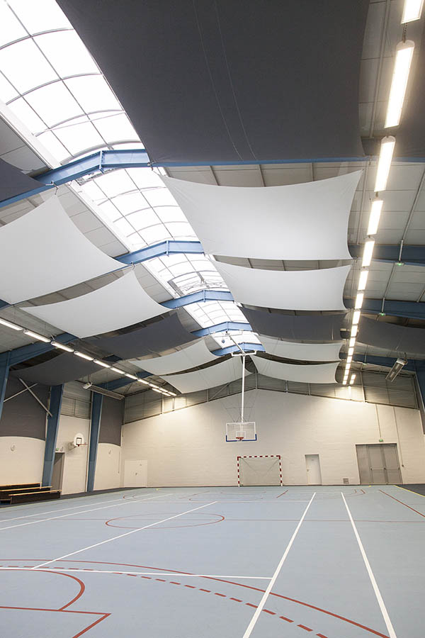 Toiles acoustiques blanches et grises accrochées au plafond d'une salle multisport