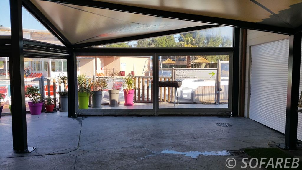 pergola vitrée noir autoportante à coté d'une porte de garage, avec beaucoup d'ombre