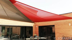 Voiles d'ombrage rouge et marron adossées à une maison en bois